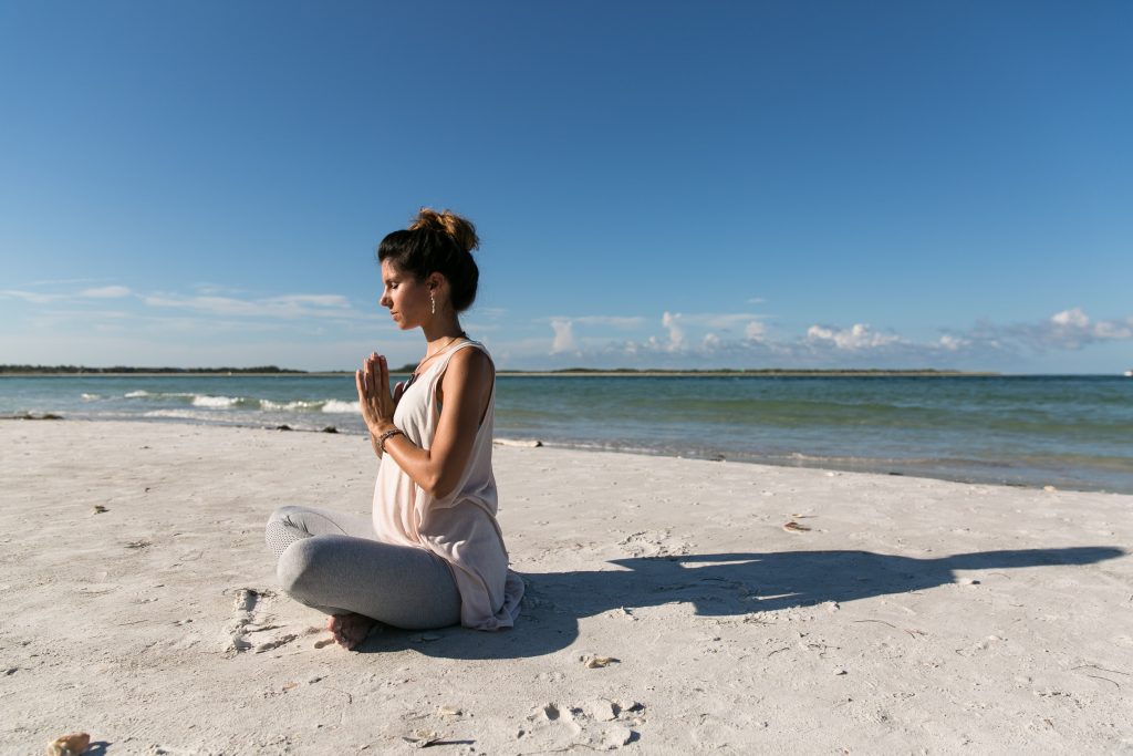 ragazza sulla spiaggia bianca con mani unite davanti al petto in meditazione
