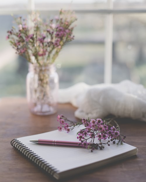 quaderno con una matita appoggiato su un tavolo con dei fiori lilla