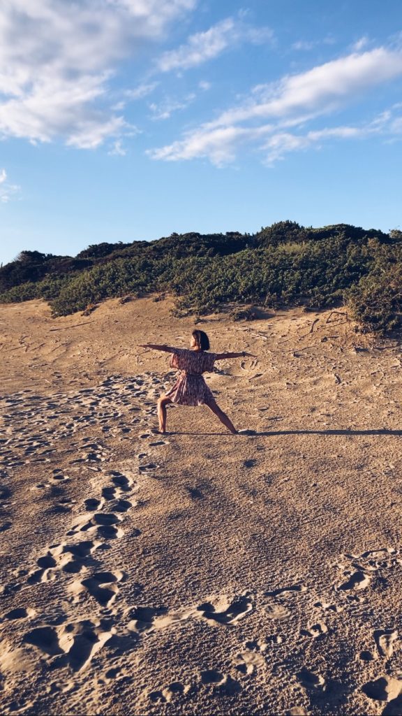 ragazza con vestito rosa nella posizione del guerriero 2 con braccia divaricate, in spiagia,. al tramonto