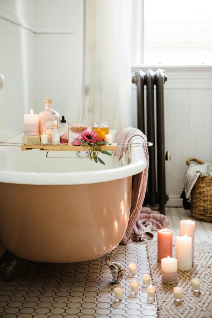 vasca da bagno con candele e prodotti di bellezza, dai colori bianco e rosa cipria
